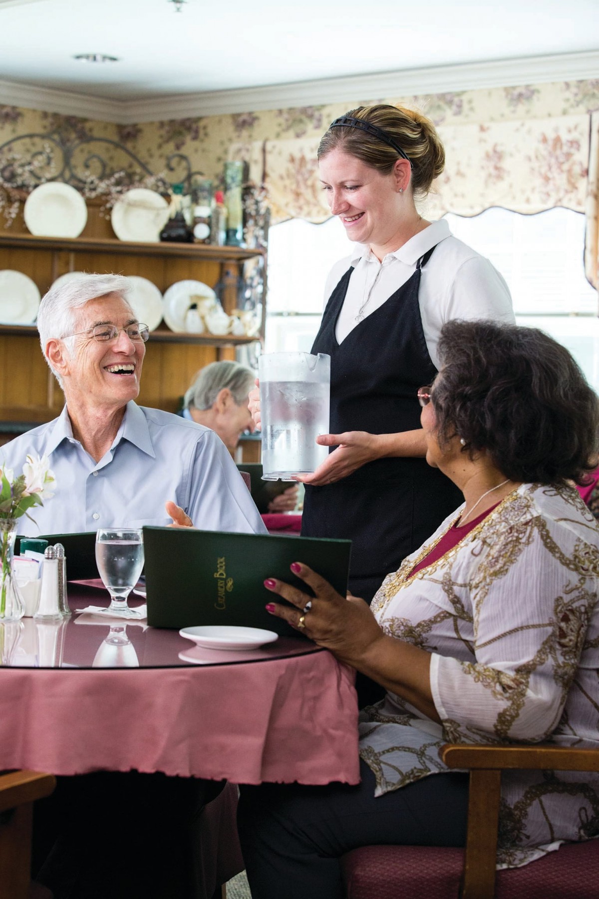 An older couple smiles and chats with a waitress while looking at menus in a restaurant.