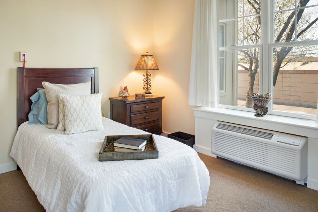 A cozy bedroom with a neatly made bed, bedside lamp, and window.