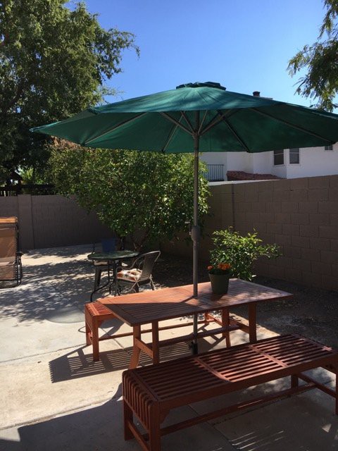 A sunny backyard patio with outdoor furniture and a green umbrella.