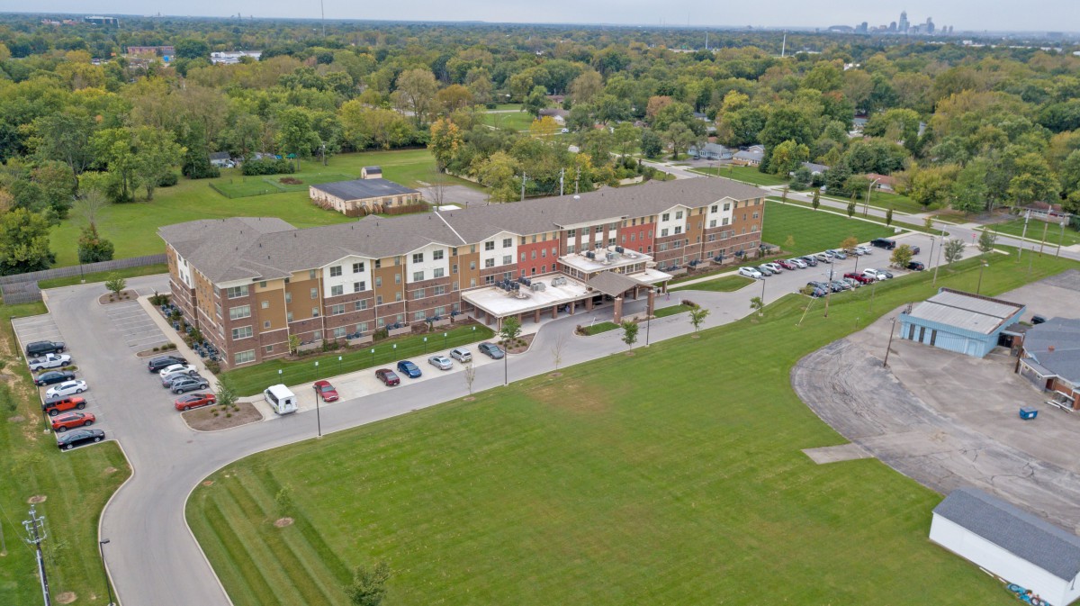 Aerial view of a hotel surrounded by lush greenery and a spacious parking lot.