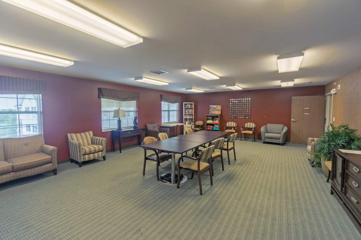 A spacious meeting room with a large conference table and chairs, surrounded by windows and comfortable seating.