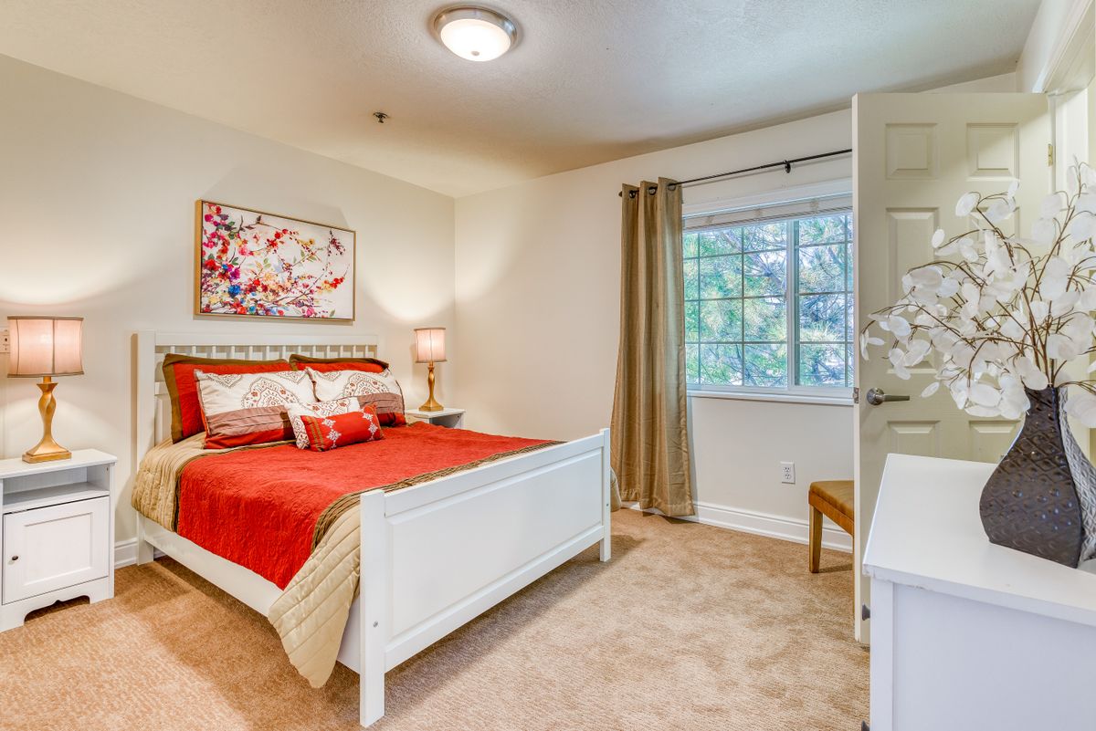 A cozy bedroom with red bedding, white furniture, and decorative artwork on the wall.