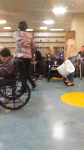 A bustling indoor area with people seated and in motion, including a person in a wheelchair.