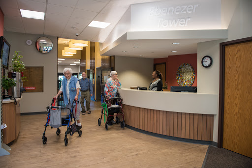 Elderly individuals entering a healthcare facility, assisted by walking aids, with staff at the reception.