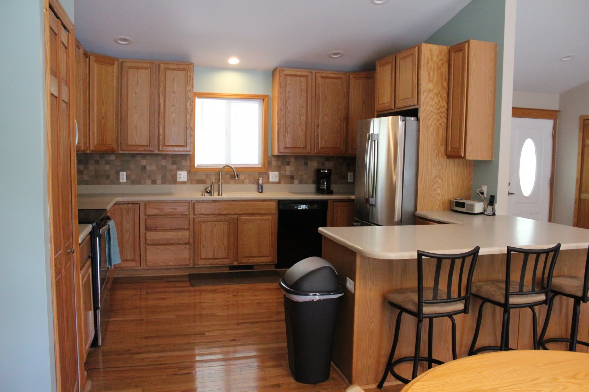 A modern kitchen with wooden cabinets, stainless steel appliances, and a central island with a bar stool.