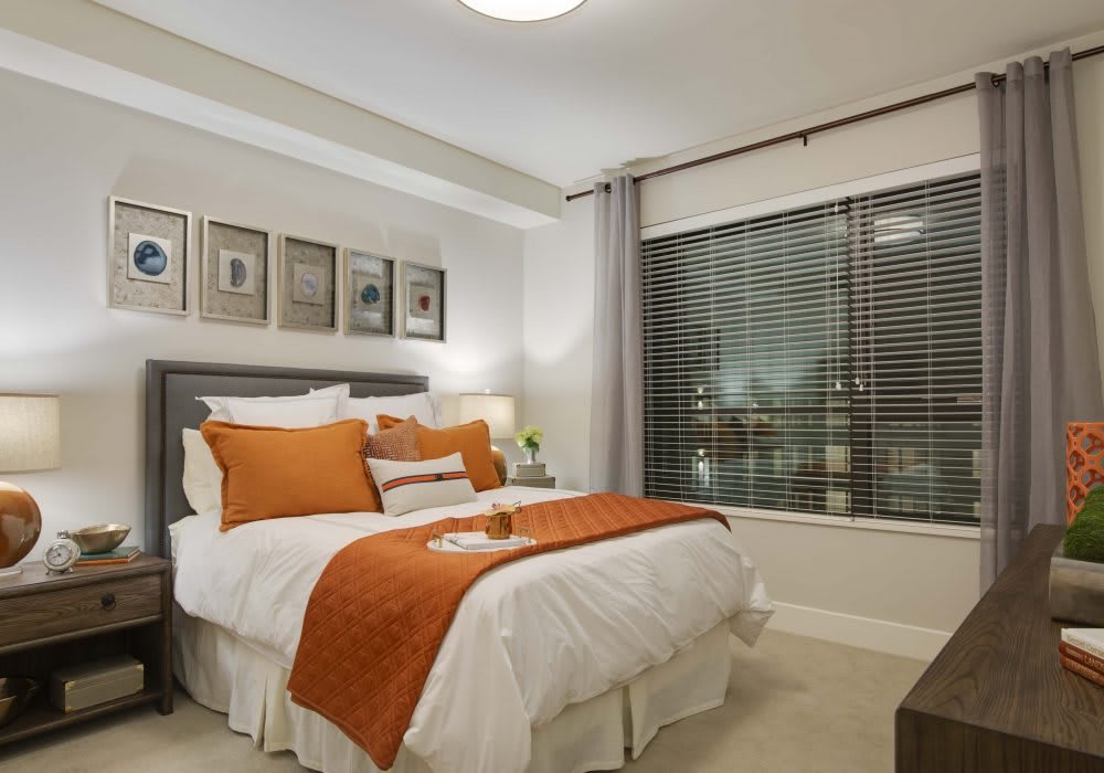 A cozy bedroom with modern decor, featuring orange accents and a large window.