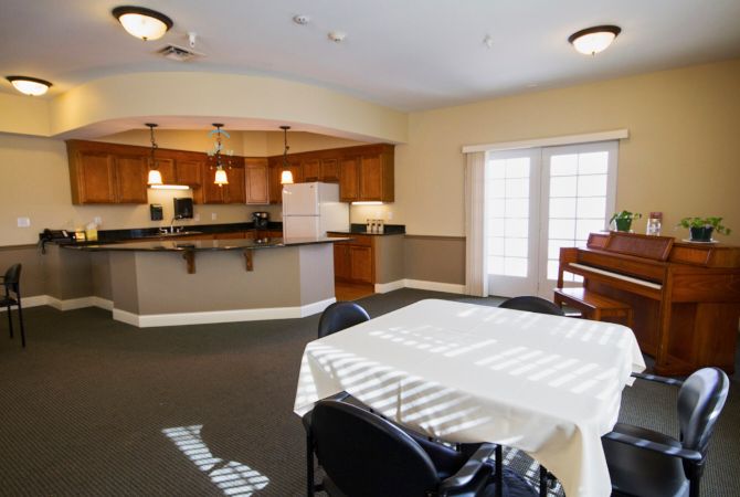 A spacious dining area and kitchen with wooden cabinetry, a white table, chairs, and a piano by the window.
