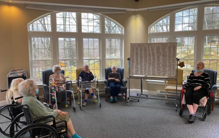 A group of elderly people sitting in wheelchairs play a game of bingo inside a well-lit room.