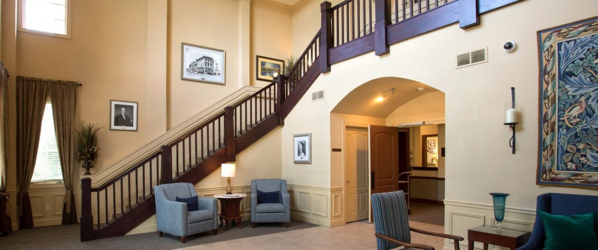 A cozy lobby interior featuring a wooden staircase, comfortable seating area, and wall decor.