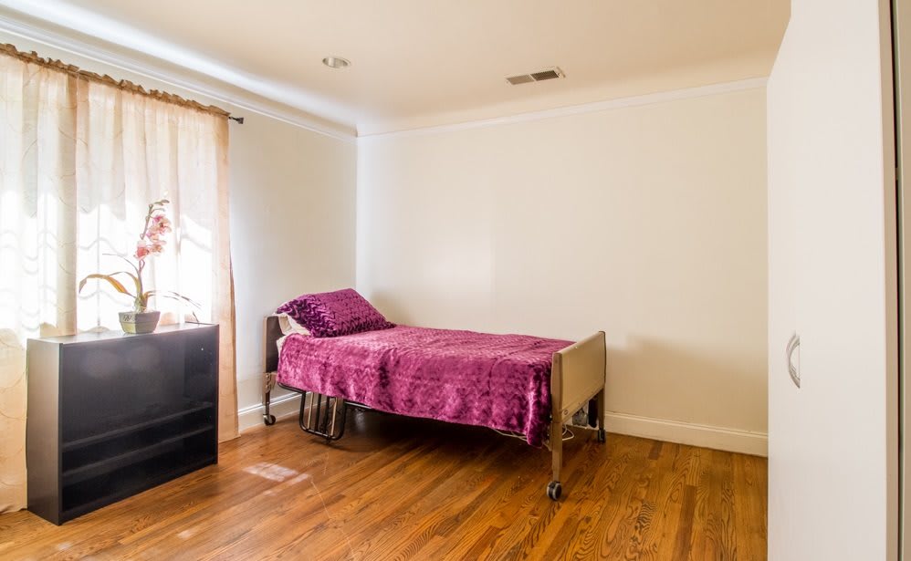 A minimalist bedroom with a single bed and pink bedding, featuring wooden floors and bright natural lighting.