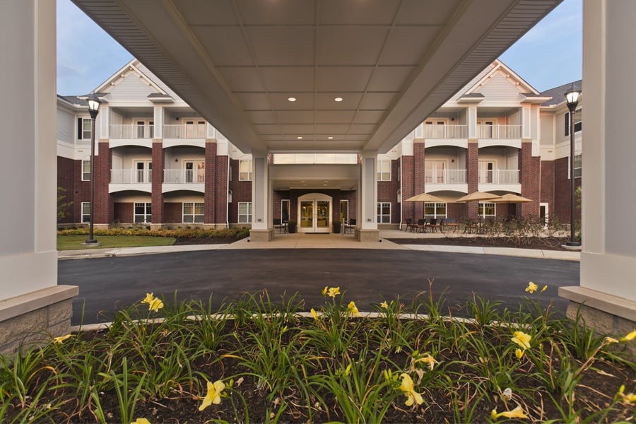 The entrance of a modern building with landscaped flowers along the pathway.