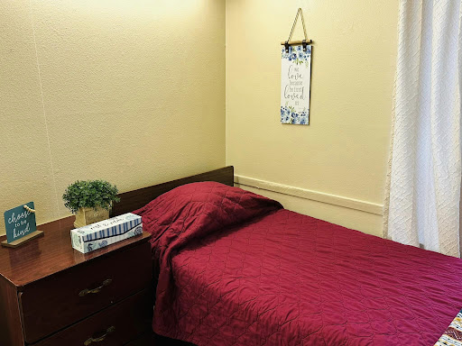 A cozy bedroom corner featuring a neatly made bed with a burgundy bedspread and a small plant on the nightstand.