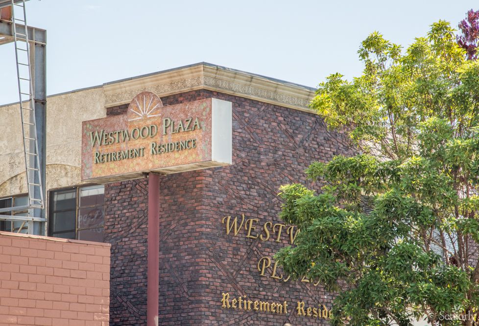A building with signage reading 'Westminster Plaza Retirement Apartments', featuring a brick exterior and surrounded by trees.