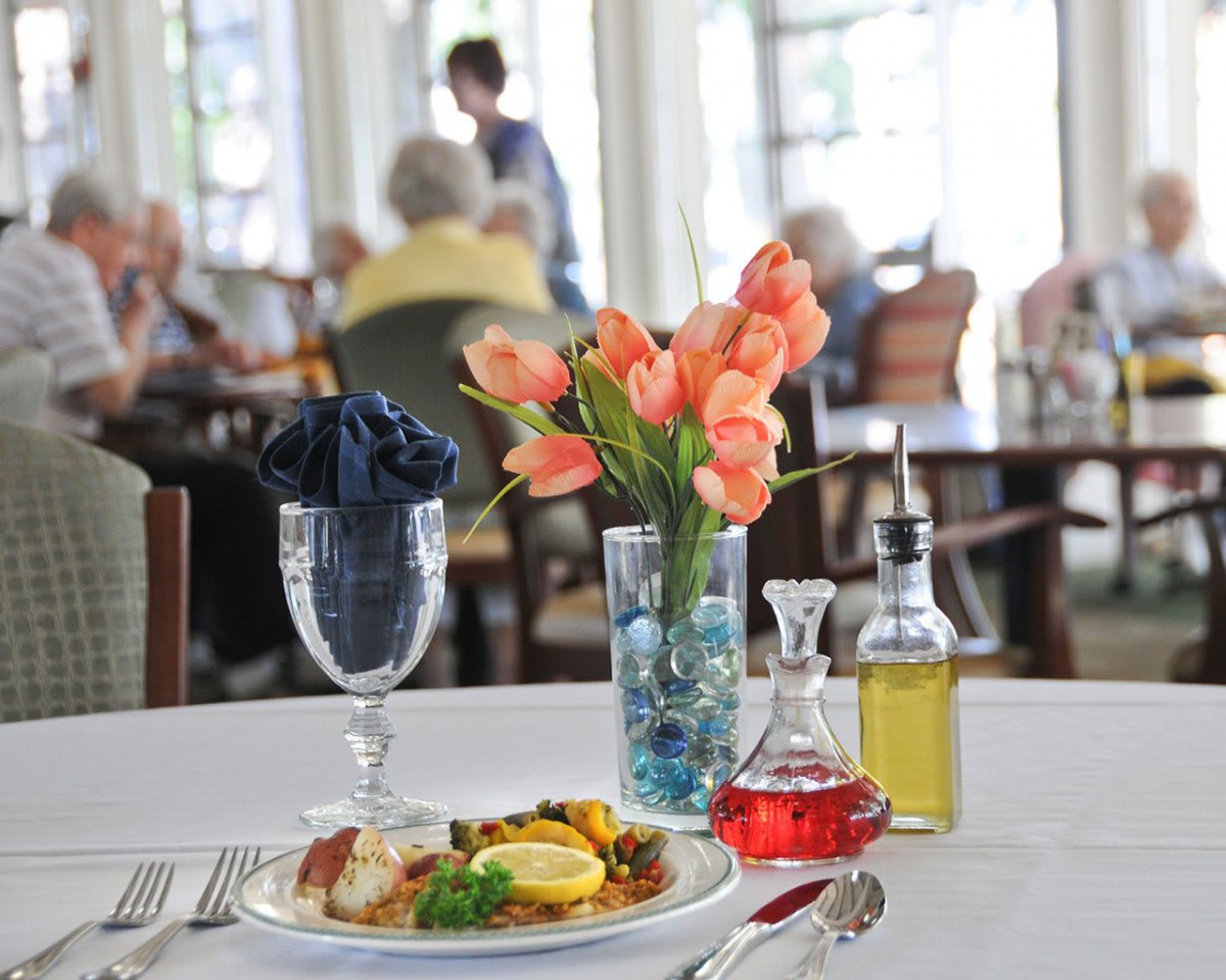 A beautifully set restaurant table with a meal, flowers, and condiments.