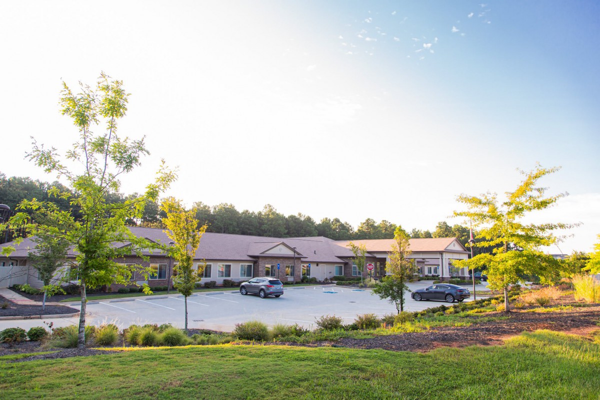 A modern building with a parking lot and surrounded by trees on a clear day.