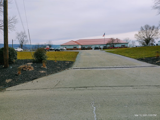 A view of a building from a long driveway, surrounded by green grass under a cloudy sky.