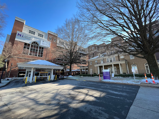 A view of a multi-story building with a canopy entrance and bare trees in the foreground under a clear blue sky.