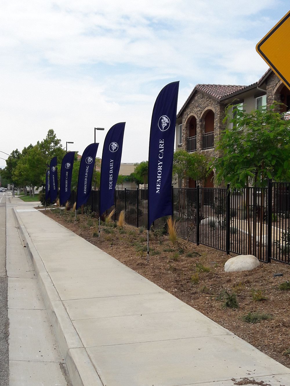 A row of promotional flags lining the sidewalk in front of an apartment complex.