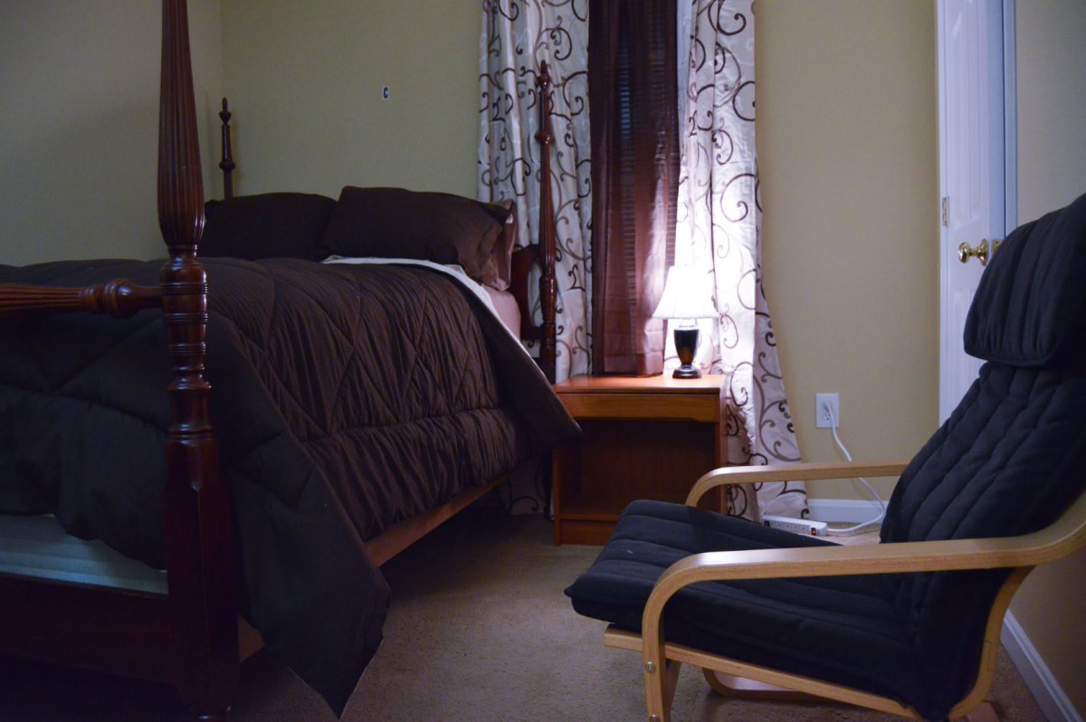A cozy bedroom with a neatly made bed, an armchair, and a lamp on the nightstand.