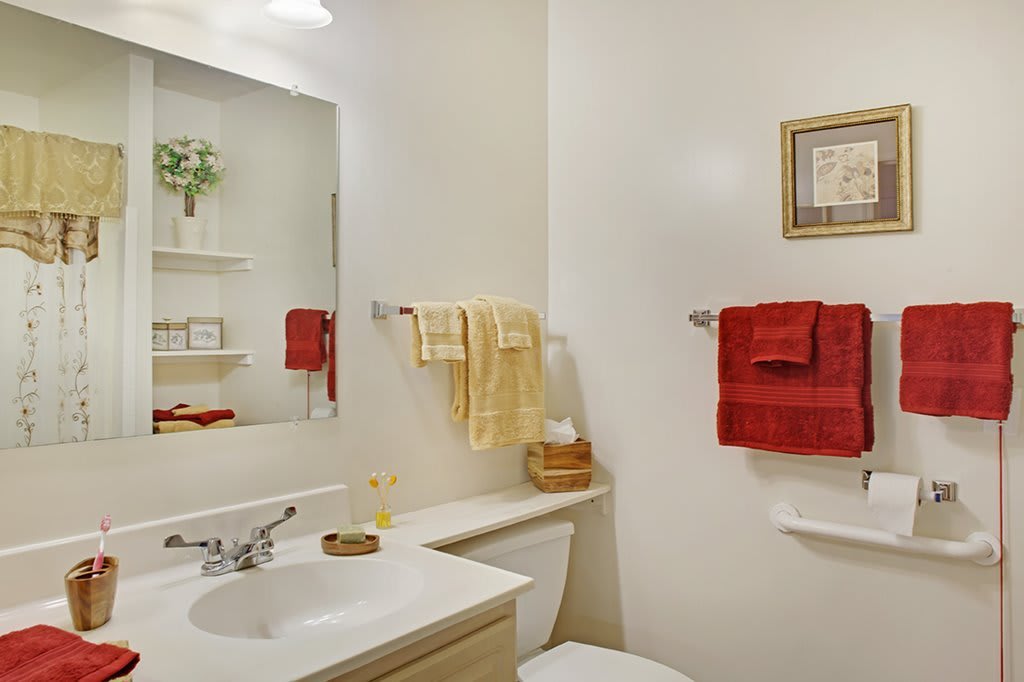 A neatly organized bathroom with red and yellow towels, a mirror above the sink, and simple decor.