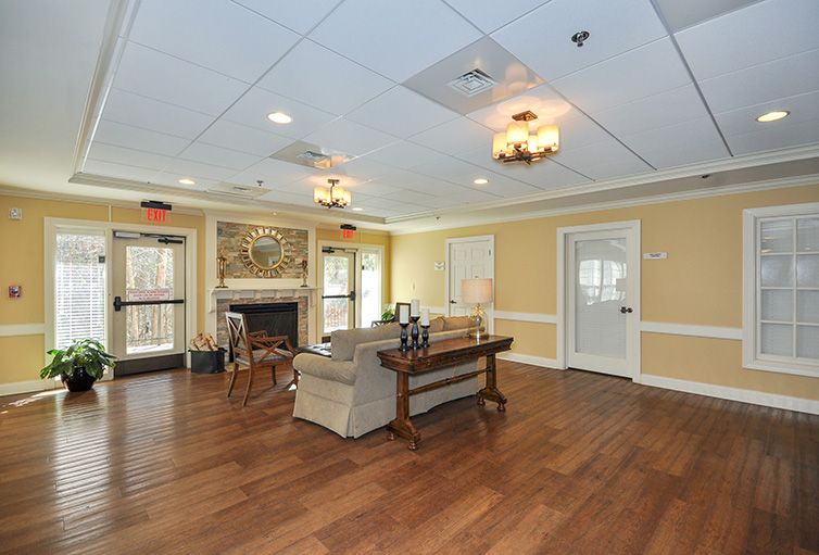 A spacious living room with wooden flooring, featuring a fireplace, comfortable seating, and chandeliers.