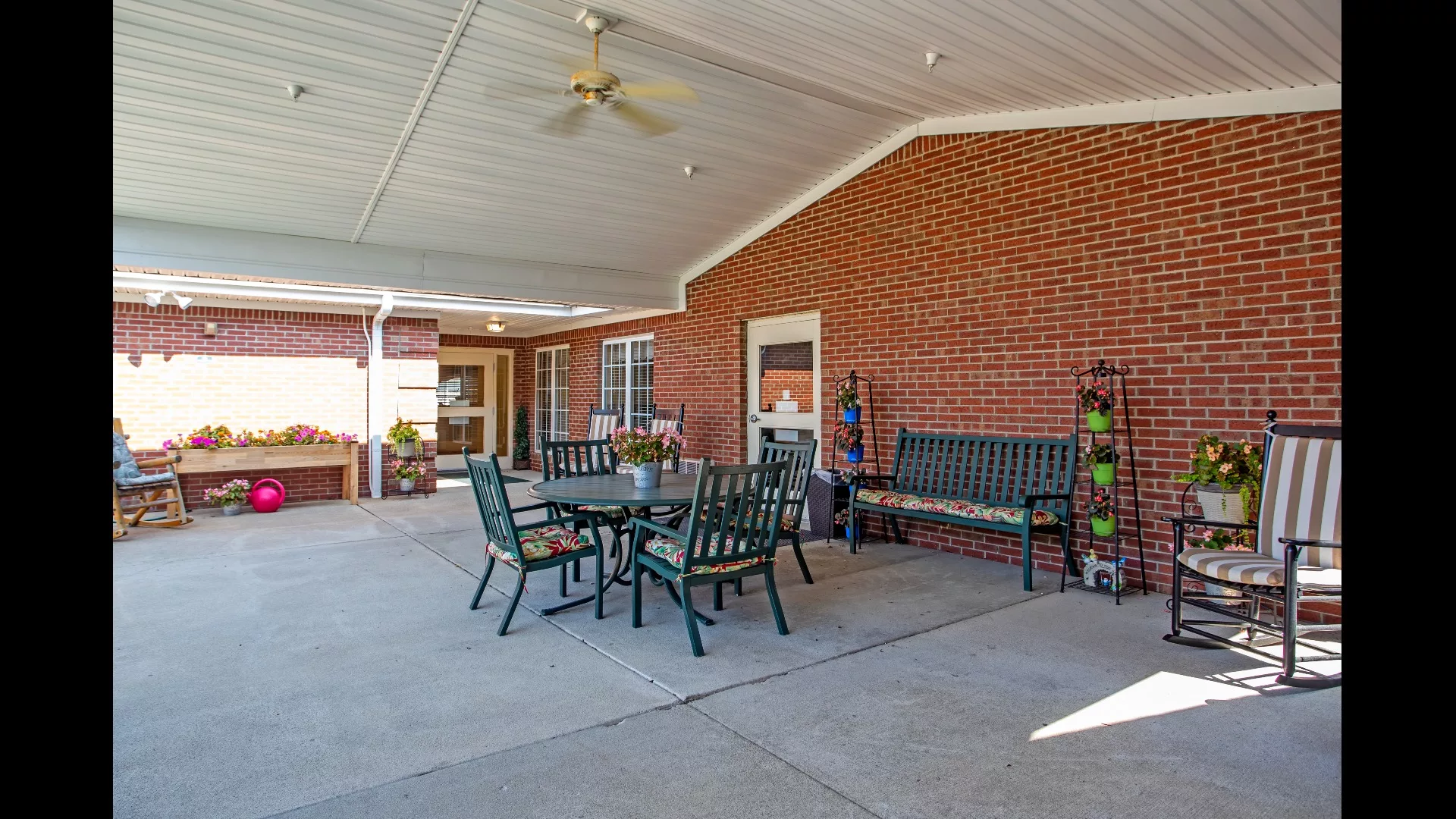A covered patio area with outdoor seating, featuring tables and chairs against a brick wall.