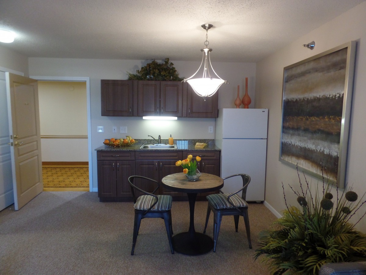 A cozy kitchen and dining area with a small table and chairs, featuring a fridge and stylish light fixture.