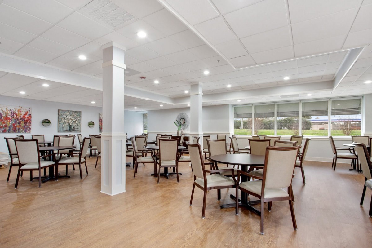 A spacious, well-lit dining area with tables and chairs arranged neatly on a wooden floor.