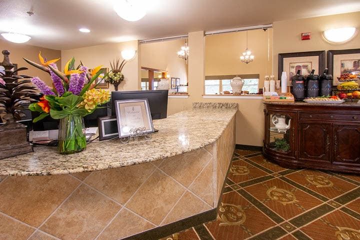 A welcoming hotel reception area with a granite desk and floral arrangement.