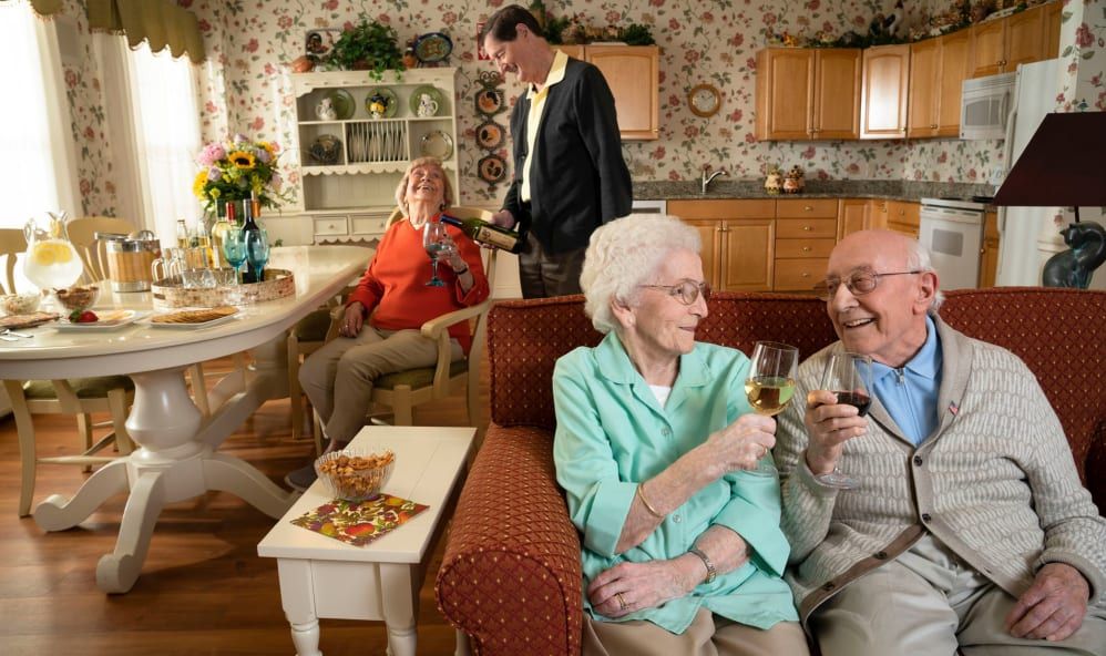 Elderly individuals enjoying a social gathering in a cozy living room while sharing drinks and smiles.