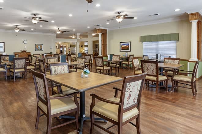 A spacious dining area with multiple tables and chairs, featuring ceiling fans and wood flooring.