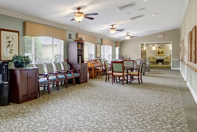 A spacious dining room with multiple tables, chairs, large windows, and ceiling fans.