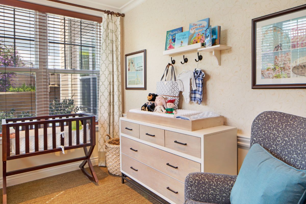 A cozy nursery with a crib, dresser, and decorative shelves near a window.