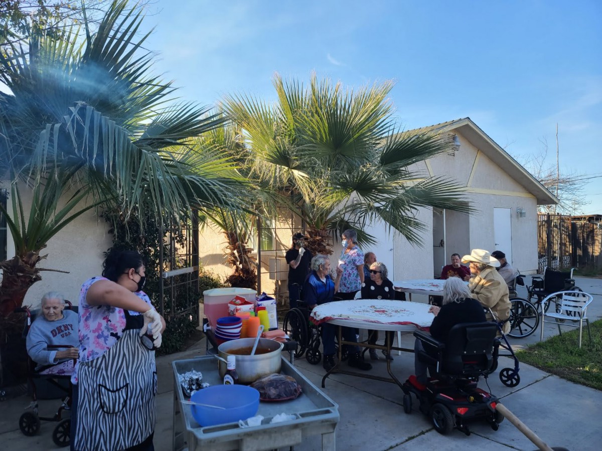 A group of people enjoying an outdoor gathering in a backyard with palm trees and a house in the background.