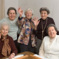 A group of elderly women smiling and waving indoors.