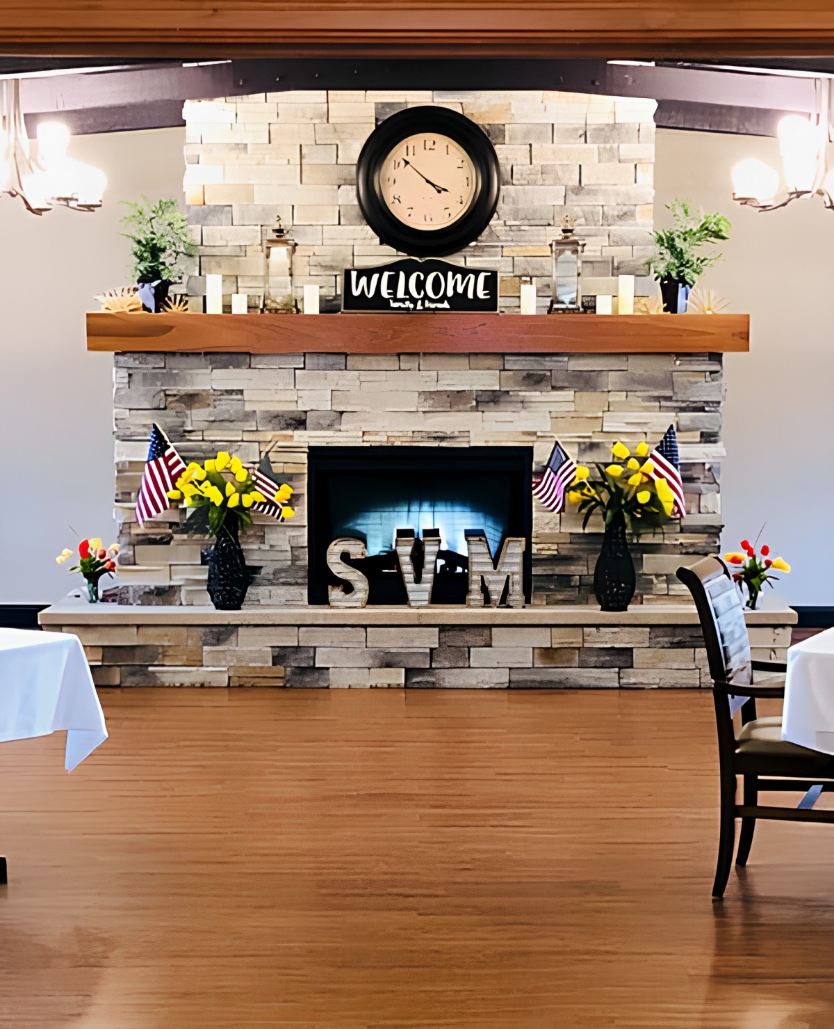 A cozy interior with a decorated fireplace, adorned with a welcome sign and surrounded by flowers and flags.