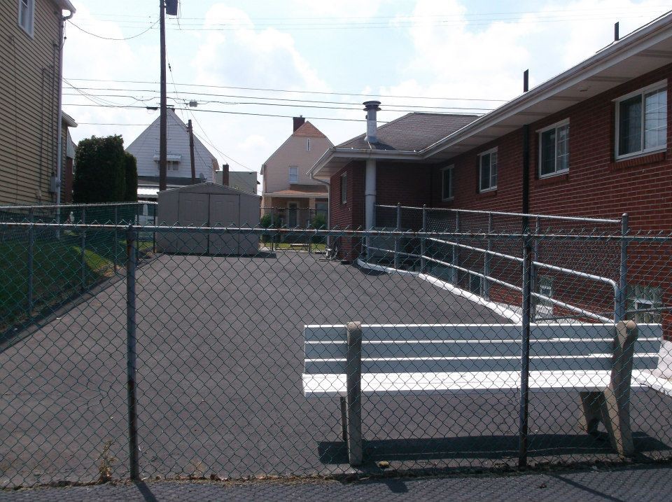 An outdoor fenced area with benches, adjacent to residential buildings.