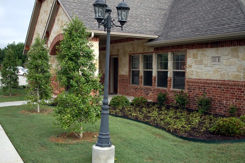 A suburban house with a brick exterior features a landscaped yard and a decorative lamp post.