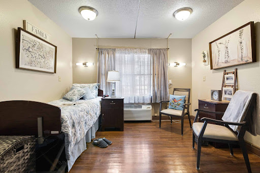A cozy and well-lit bedroom featuring a bed, chair, and natural light from the window.