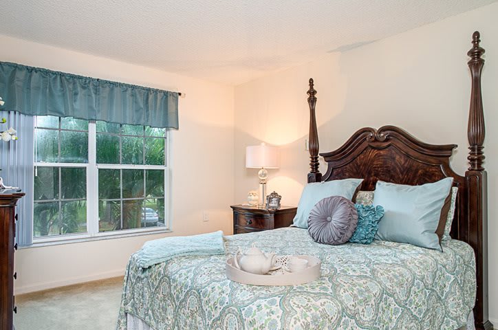A cozy bedroom featuring a large bed with patterned bedding, a bedside table with a lamp, and a window with curtains.
