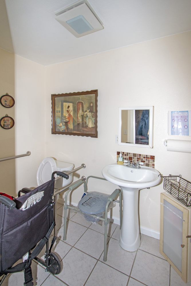 An accessible bathroom equipped with a wheelchair, handrails, and a pedestal sink beneath a mirror.