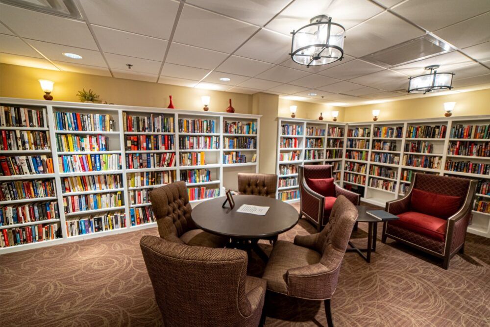 A cozy library corner featuring bookshelves filled with books, comfortable chairs, and a round table.