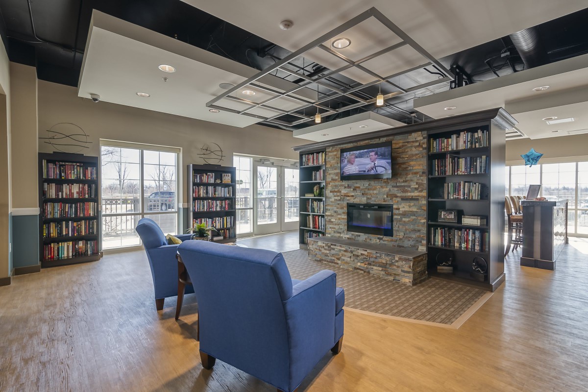 A modern library with comfortable seating, a stone fireplace, and bookshelves lining the walls.