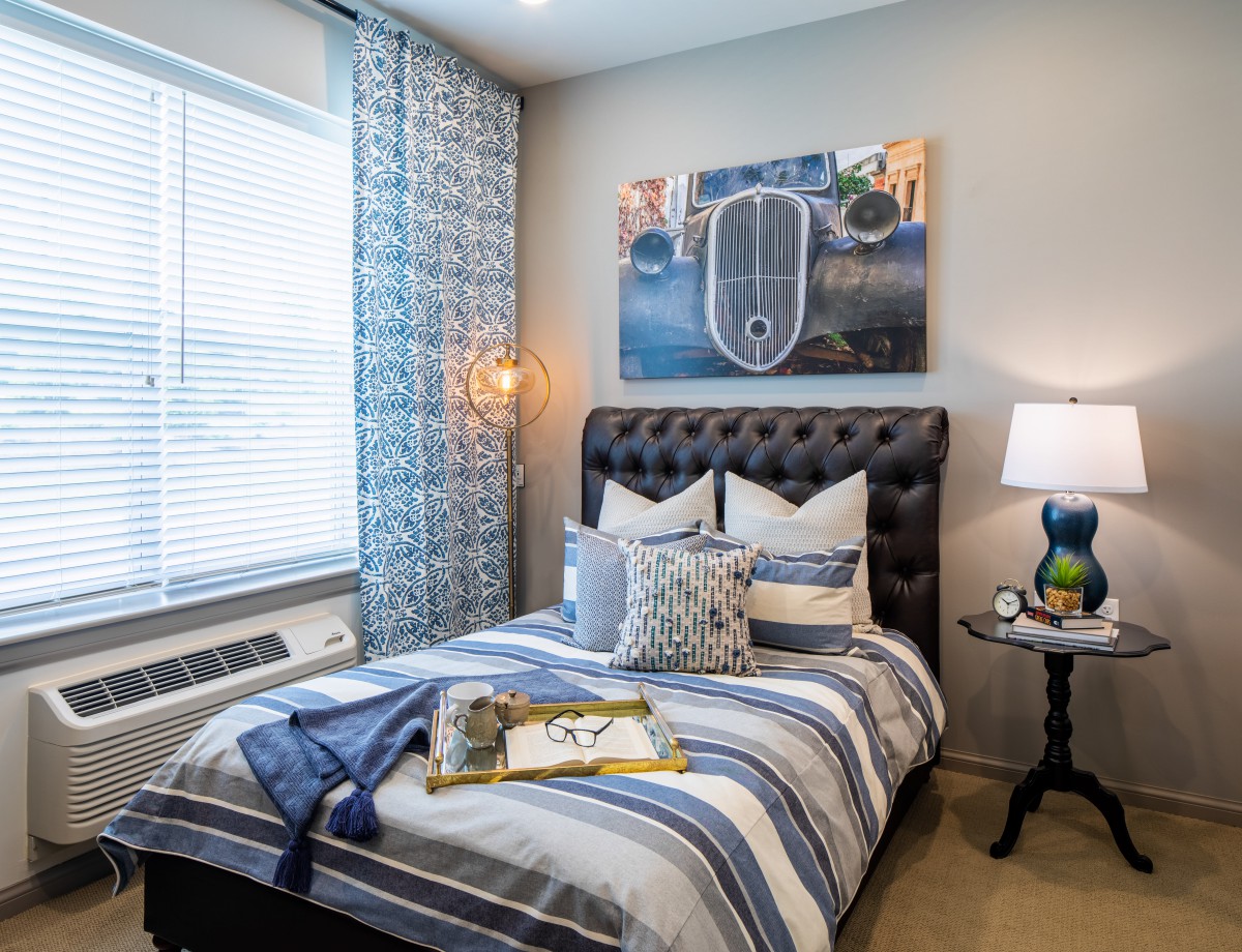A cozy bedroom featuring striped bedding, decorative pillows, and a stylish lamp beside a tufted headboard.