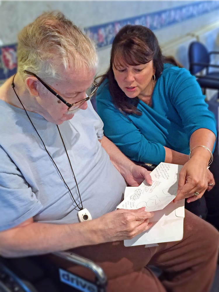 An older man receives help and guidance with paperwork from a woman.