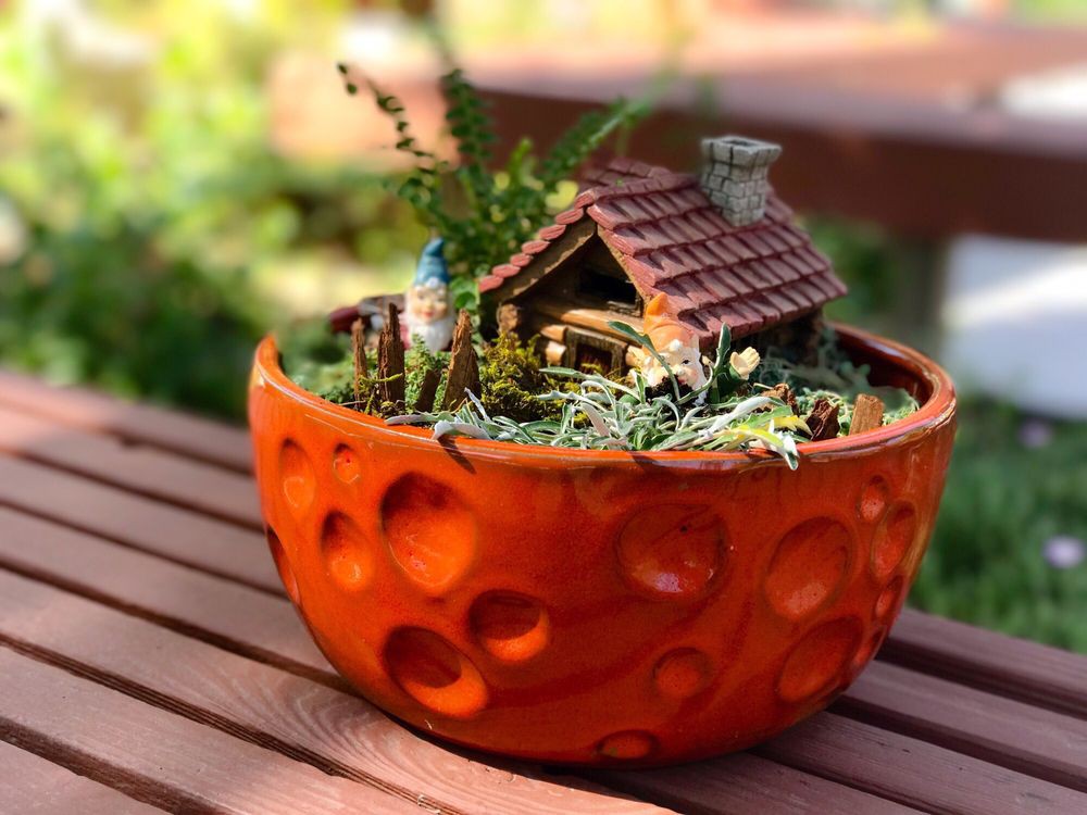 A charming miniature garden with a wooden house model in a decorative orange planter.