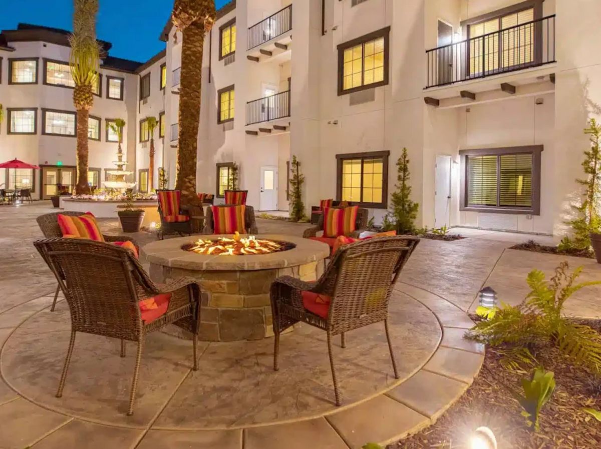 A cozy outdoor courtyard with a fire pit surrounded by chairs, illuminated in the evening.