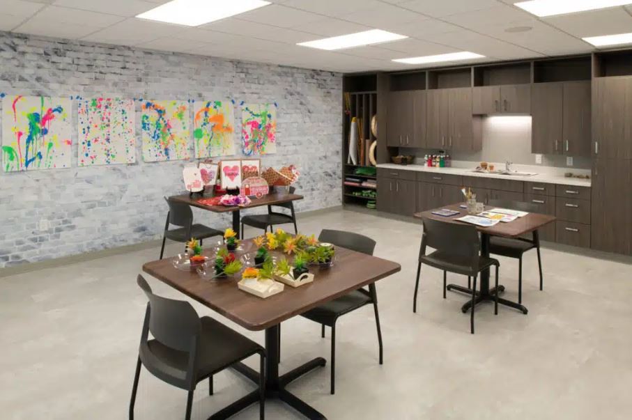 A modern workspace featuring tables and chairs with colorful artwork on the wall.