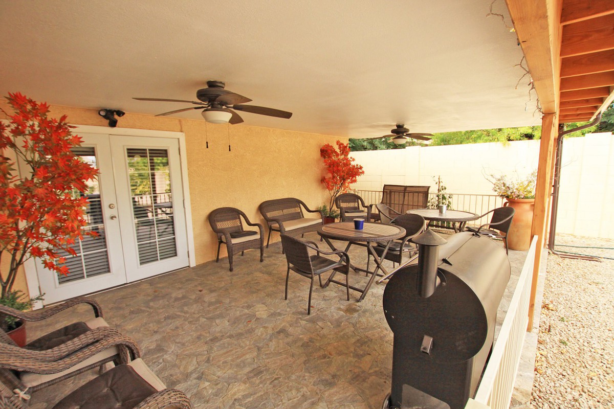 A cozy covered patio with tables, chairs, ceiling fans, and a barbecue grill.