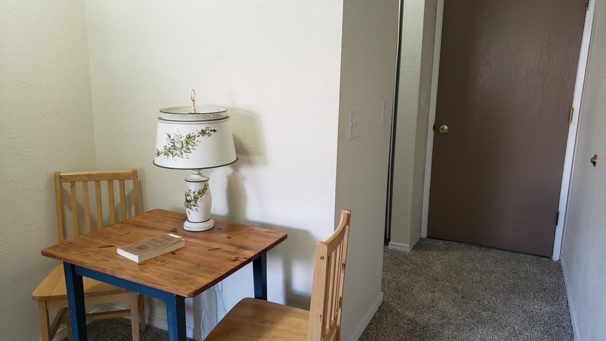 A small wooden table with a floral lamp and an open notebook beside it, positioned next to a doorway.